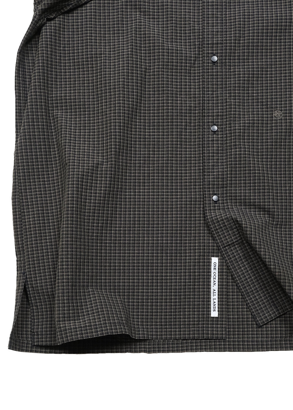 Close-up of a dark charcoal gray and navy checkered button-down shirt, showing the fabric texture, button details, and a white brand label on the sleeve cuff.