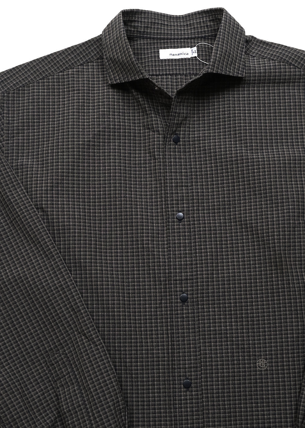 A close-up of a dark charcoal gray and navy checkered button-down shirt, showing the collar, front buttons, and a small embroidered logo on the lower right chest.